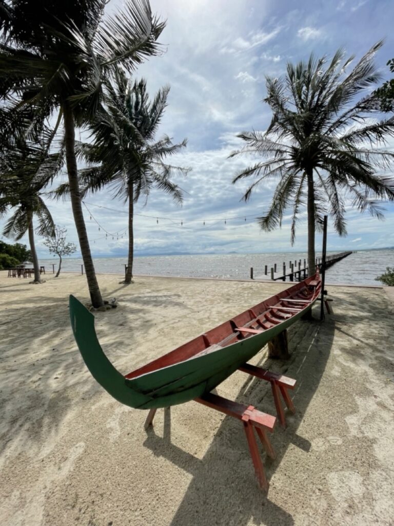 a Khmer pirogue by the sea with palm trees and blue sky